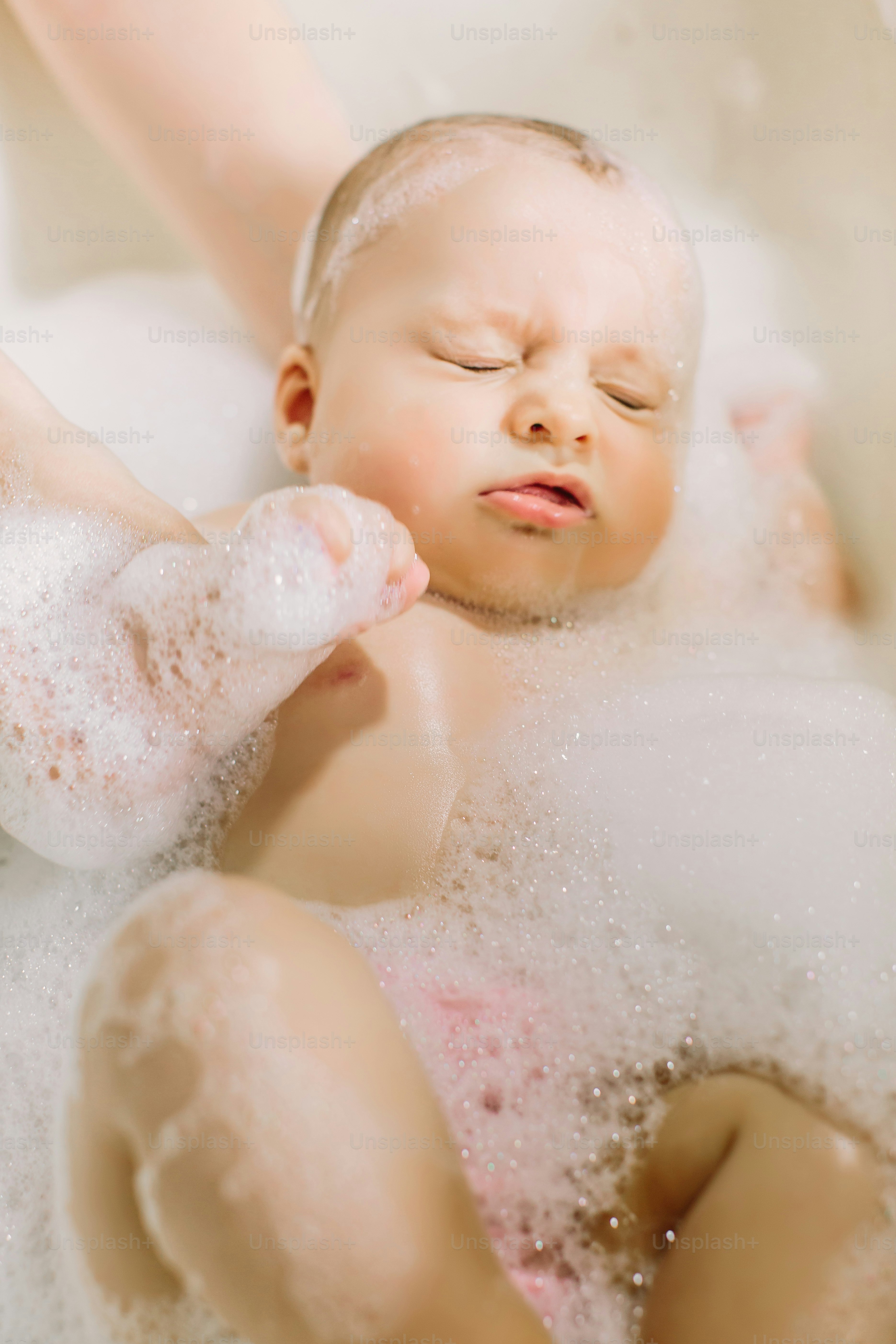 Happy laughing baby taking a bath playing with foam bubbles. Little