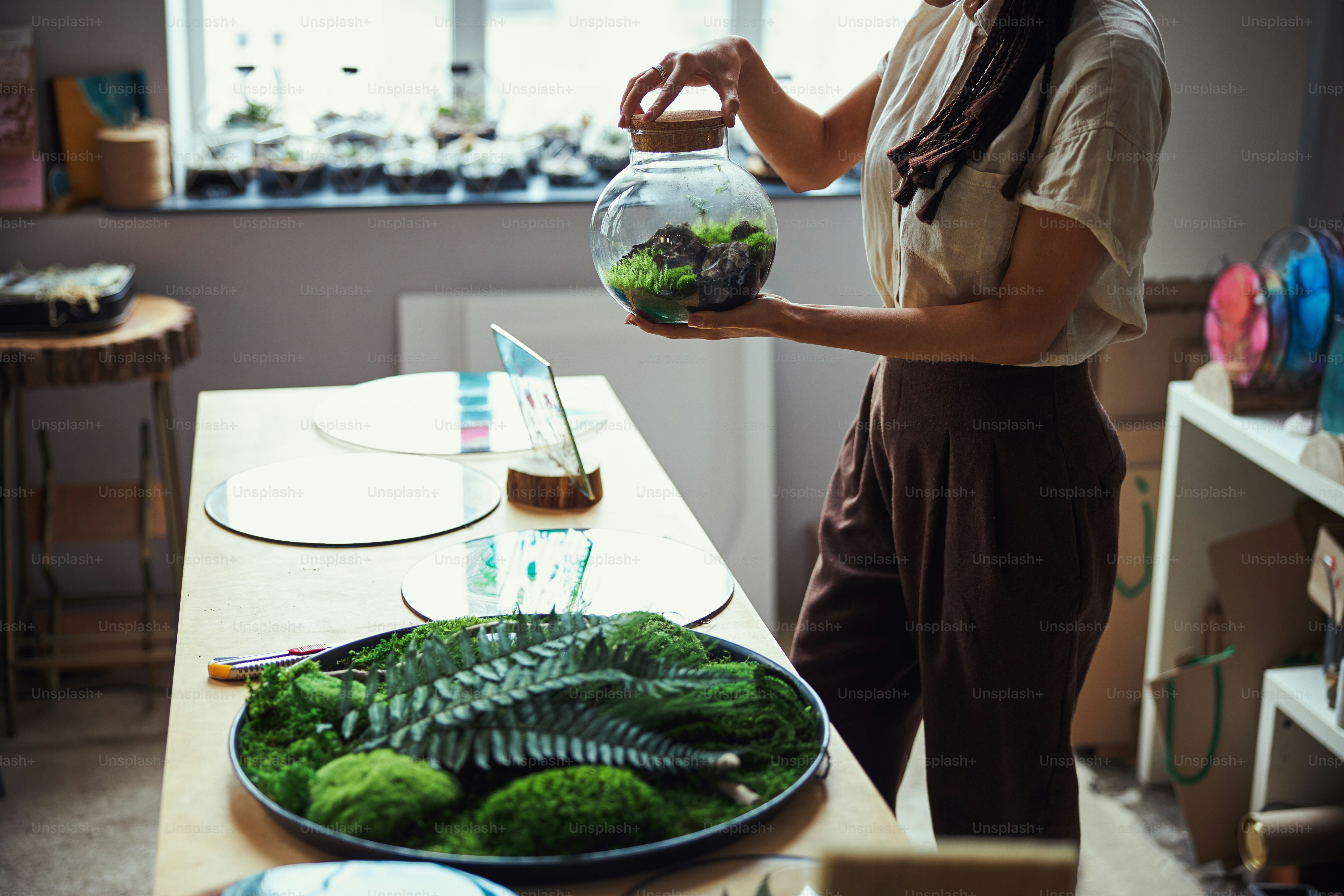 Cropped photo of a certified florist holding a closed round glass jar