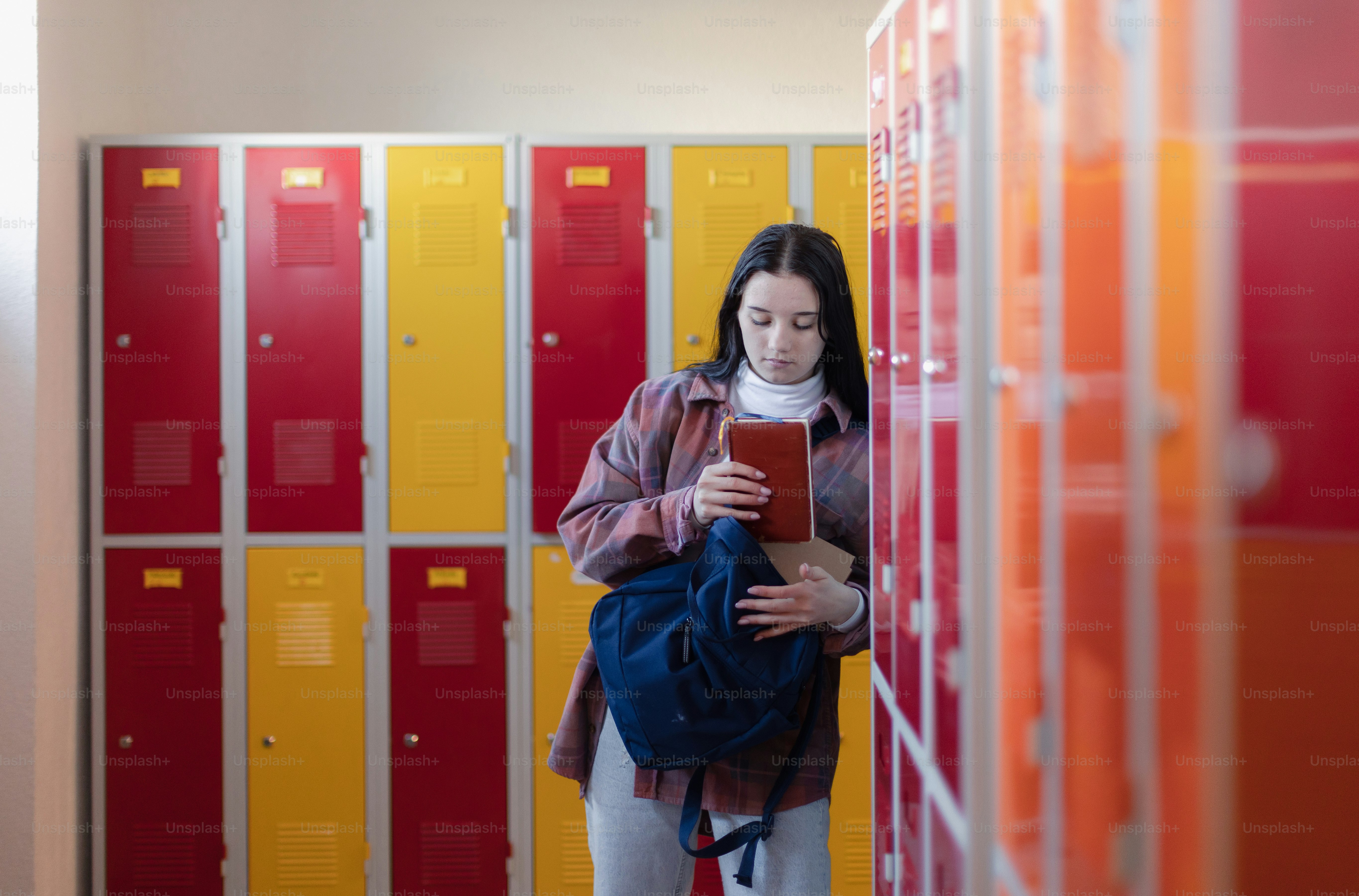A teenage student sitting in corridor near colorful lockers adn packing