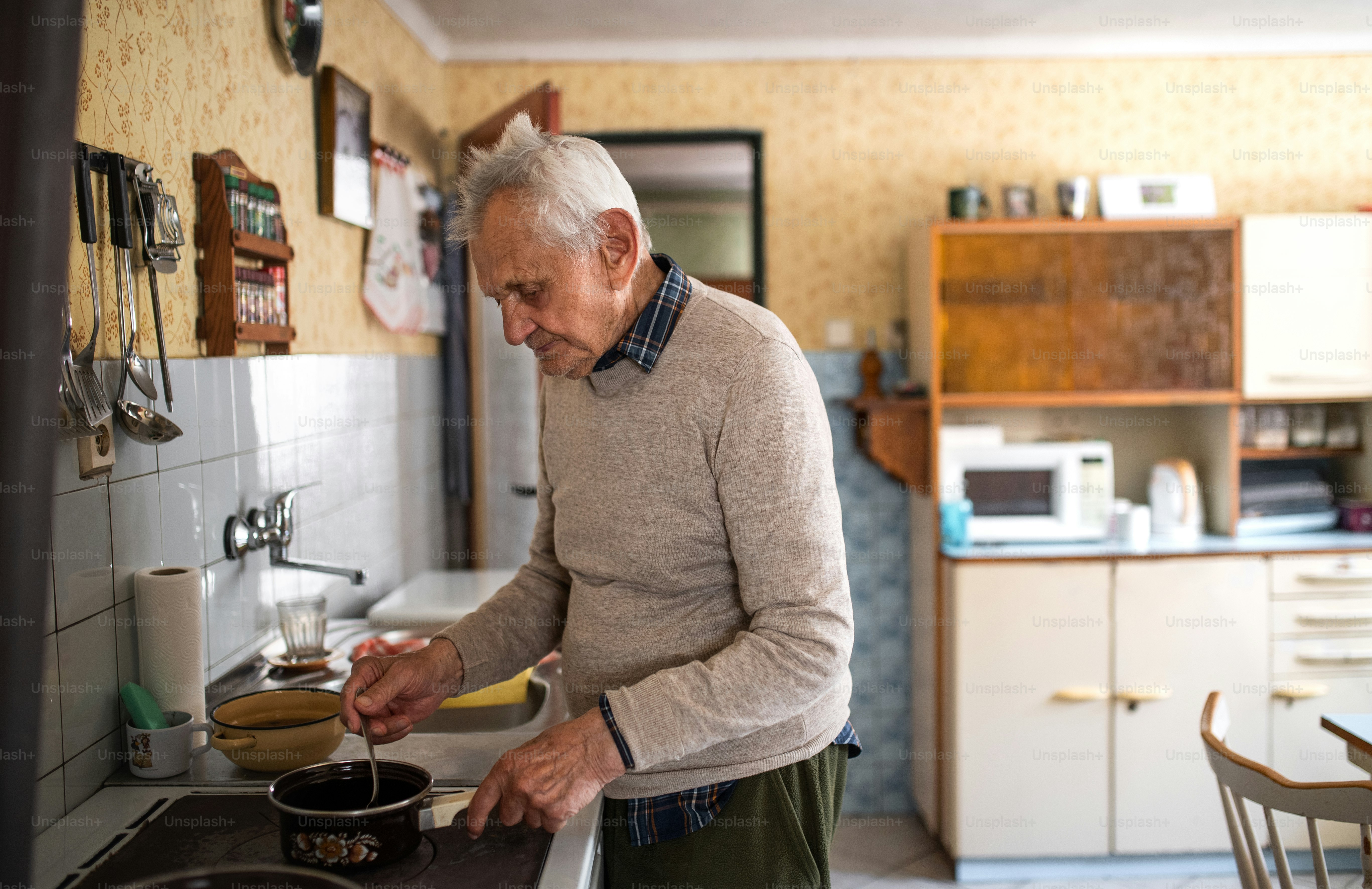 A portrait of elderly man cooking on stove indoors at home, stirring