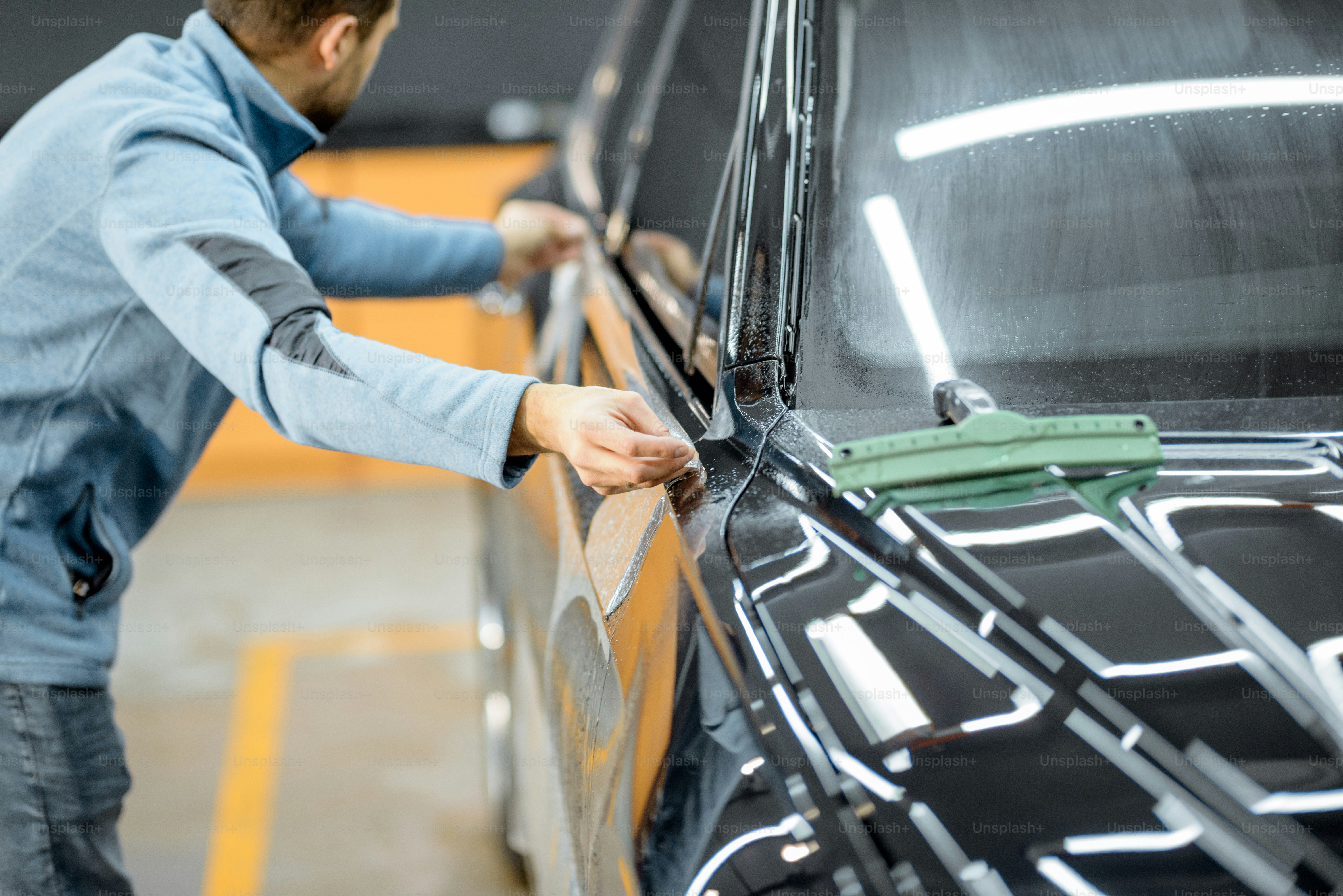 Car service worker sticking antigravel film on a car body for