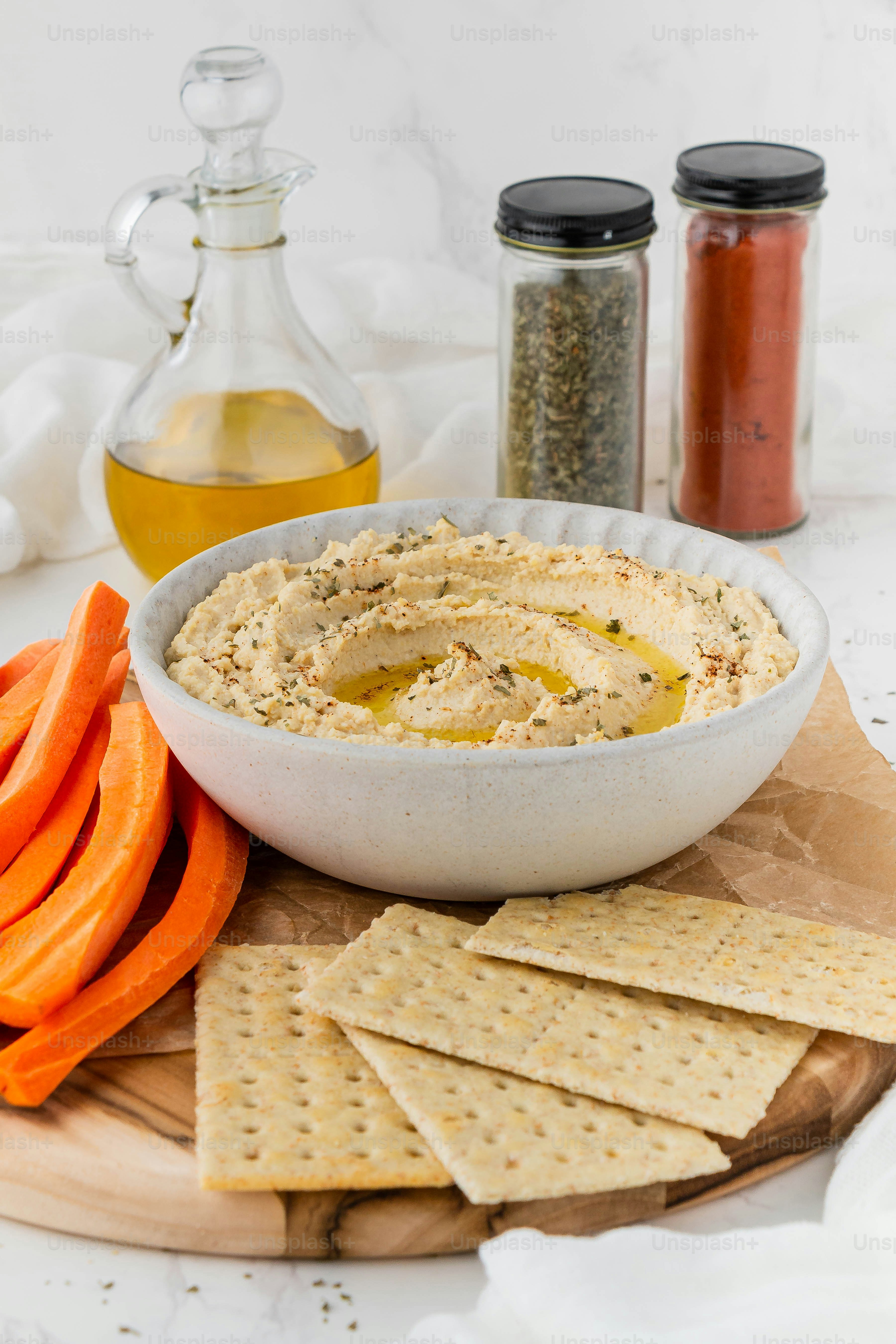 A bowl of hummus, carrots, and crackers on a cutting board photo Food