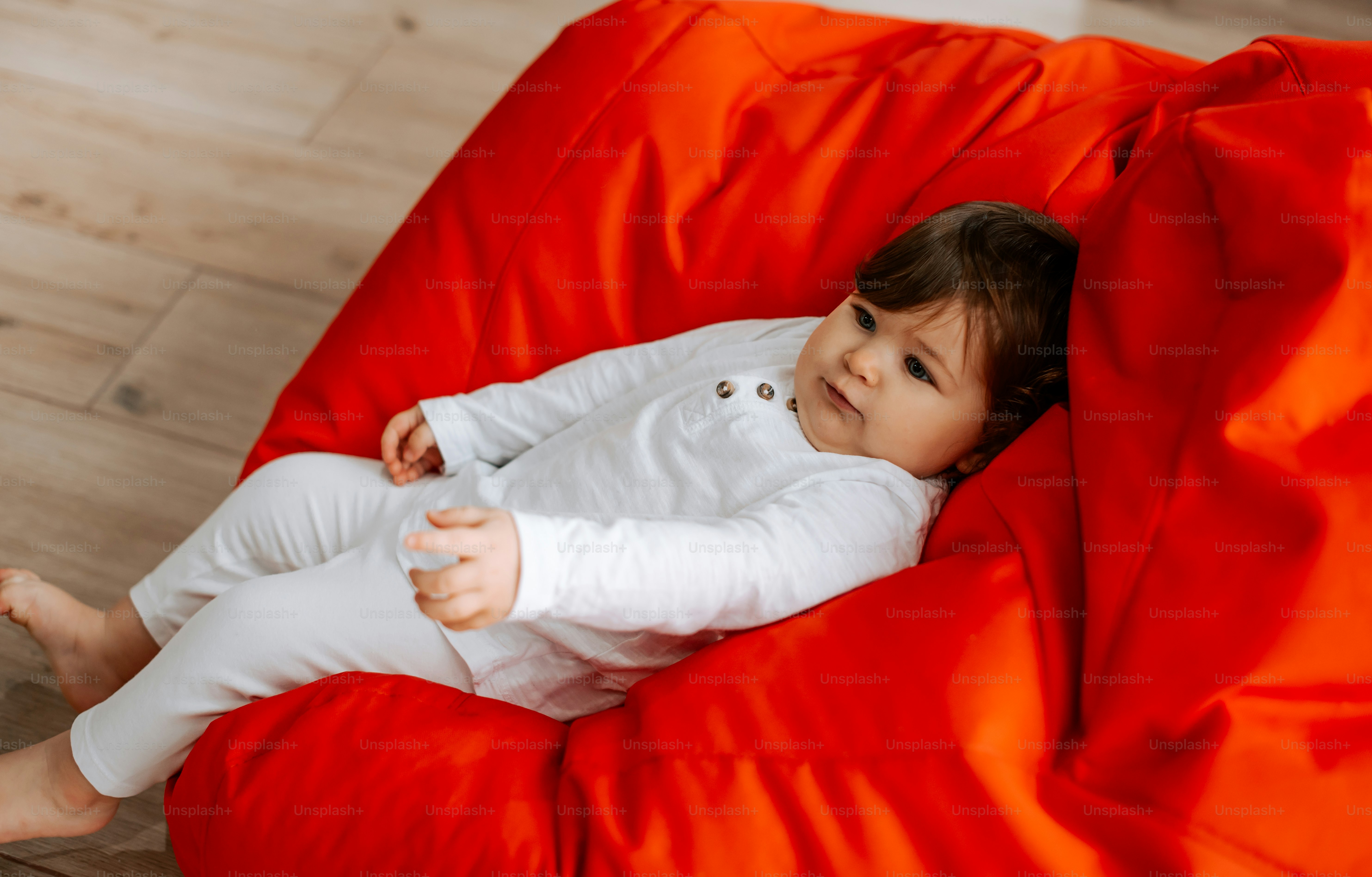 A baby sitting on a red bean bag chair photo Everyday moments Image