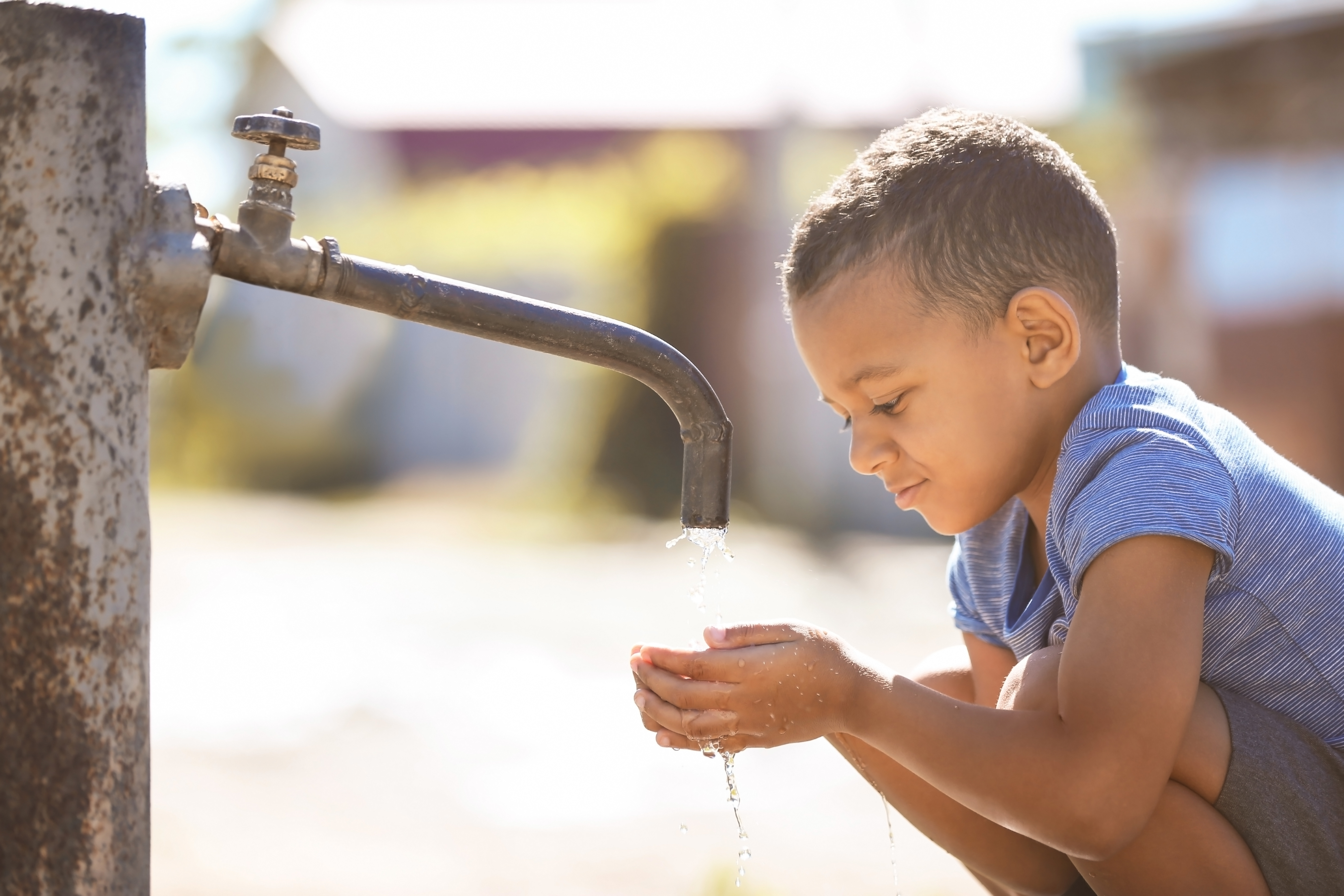 African American child drinking water from tap outdoors. Water scarcity