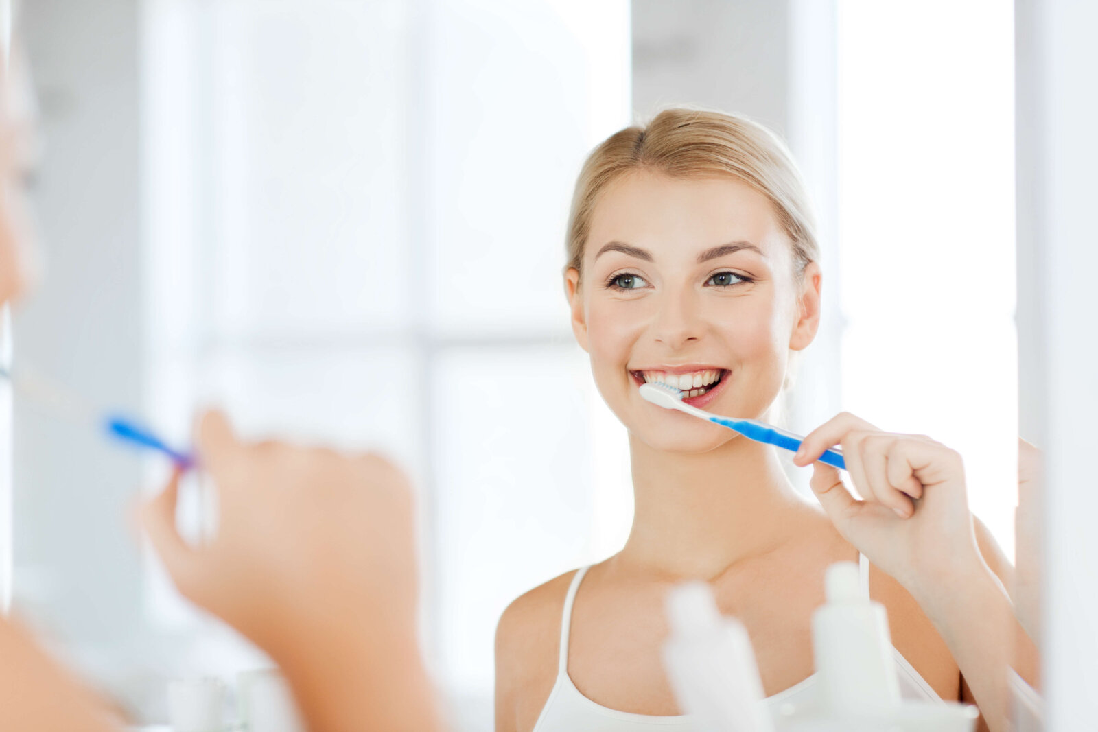 woman with toothbrush cleaning teeth at bathroom Hancock Village Dental