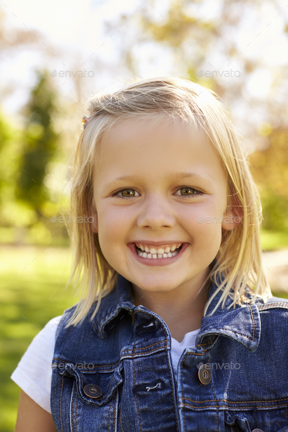 Five year old blonde girl in park smiles to camera, vertical Stock