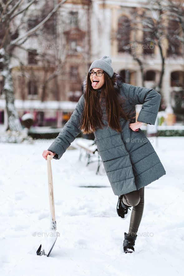 Beautiful girl in winter fashion clothes with a shovel Stock Photo by