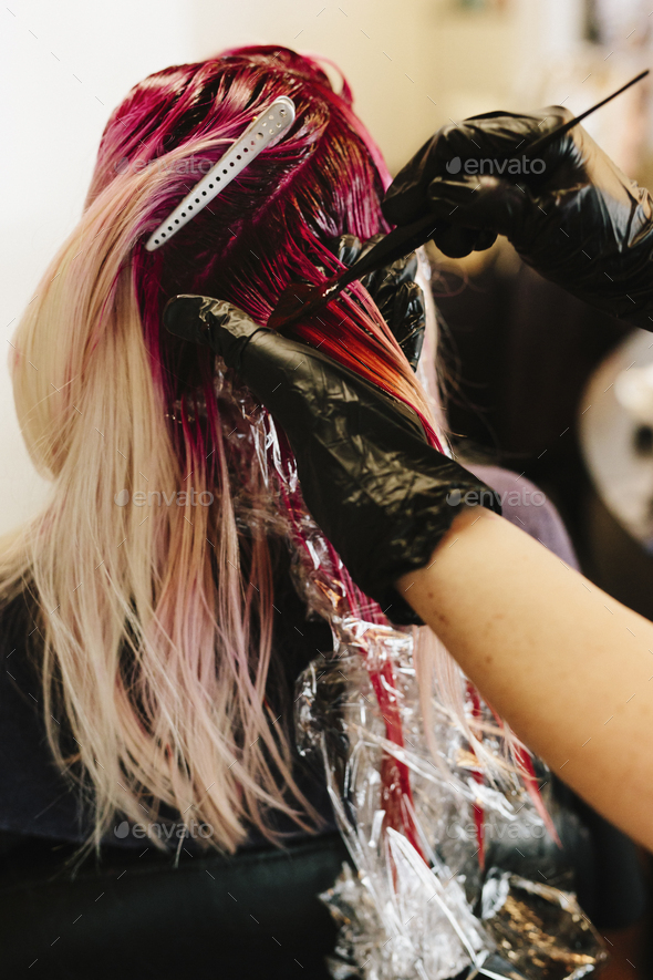 A hair colourist applying pink hair colour to a client's long blonde hair. Stock Photo by Mint