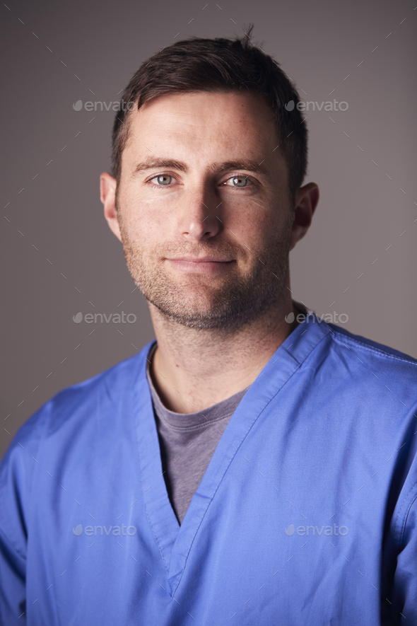 Studio Portrait Of Male Nurse Wearing Scrubs Standing Against Grey