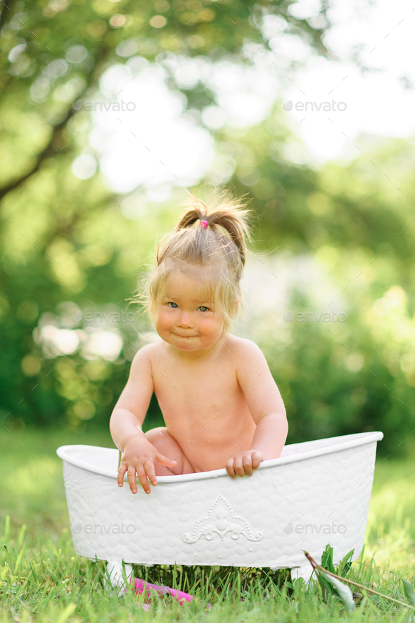 Happy toddler girl takes a milk bath with petals. Little girl in a milk