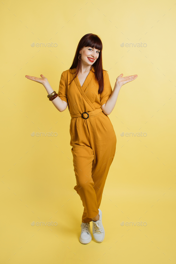 girl in yellow overalls and sneakers, posing on isolated pastel yellow