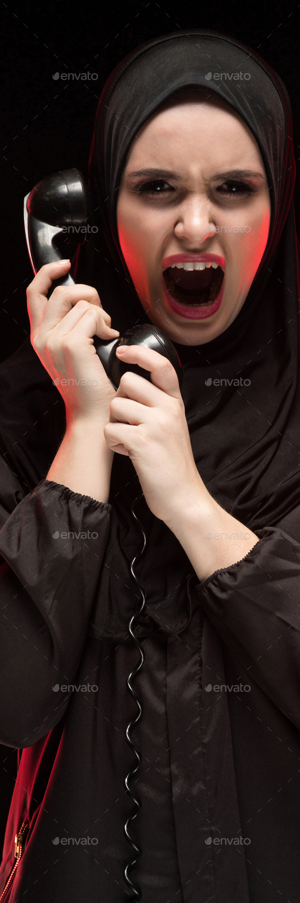 Portrait of beautiful serious scared young muslim woman wearing black hijab screaming calling