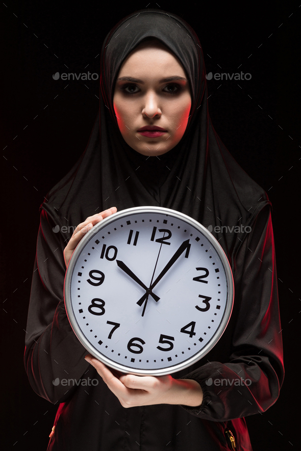 Portrait of beautiful serious scared frightened young muslim woman wearing black hijab holding