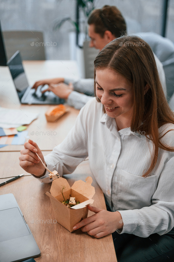 Two coworkers are eating food that is in the eco boxes. Sitting in the