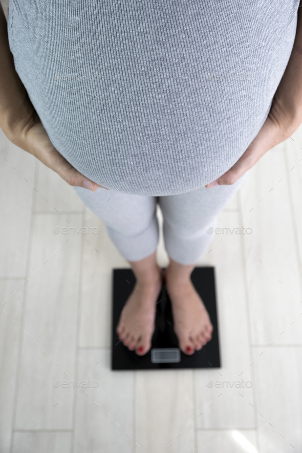 Pregnant woman on scales at home check her weight gain. Weight control