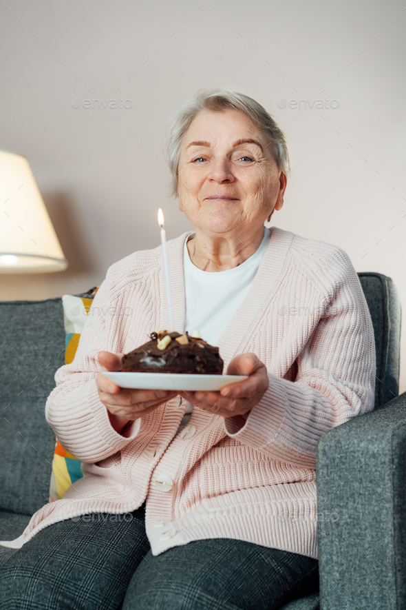 smiling mature aged senior woman holds birthday cake and blowing a