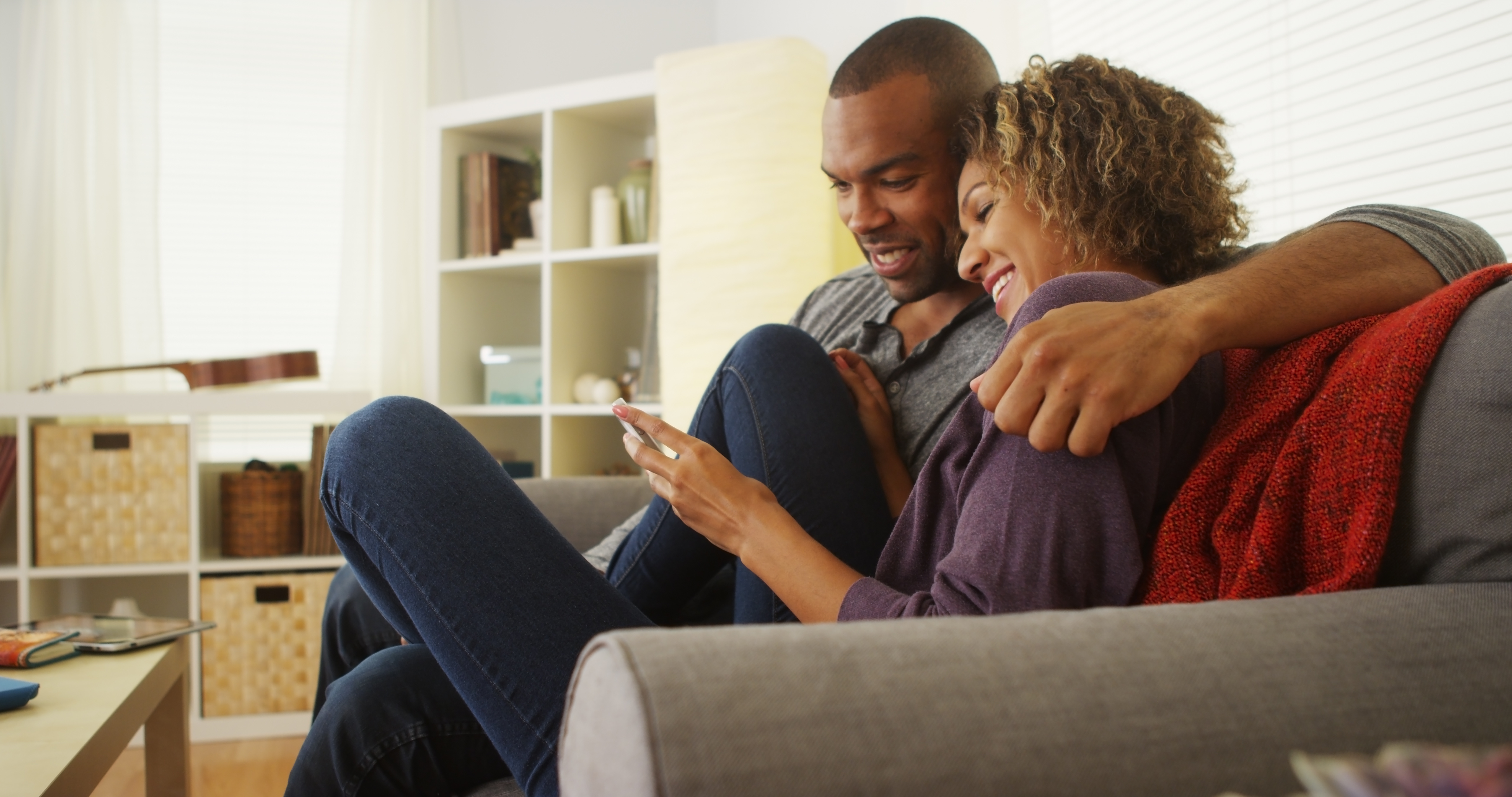 African American couple using devices on couch Sceptre Mortgage