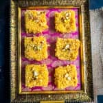 6 pieces of mango kalakand placed on a pink and golden tray