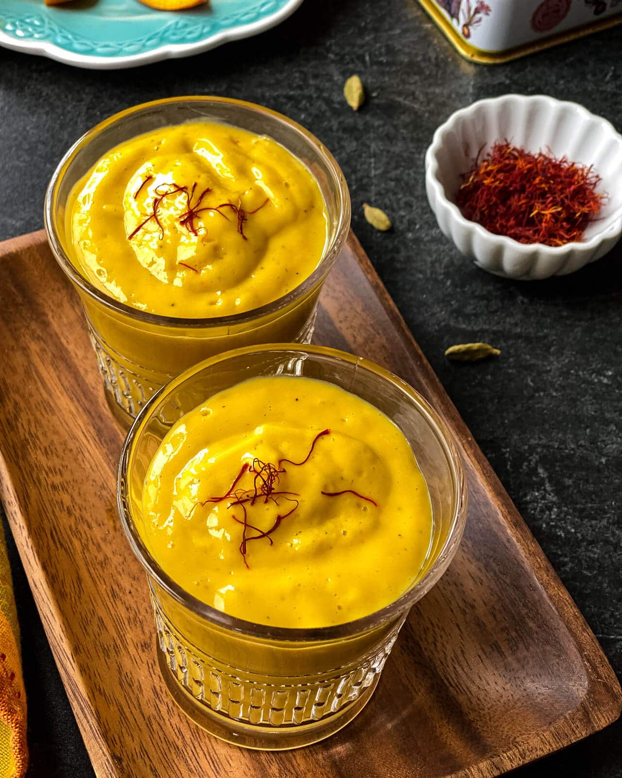 An overhead shot of two glasses of Mango lassi served on a wooden tray