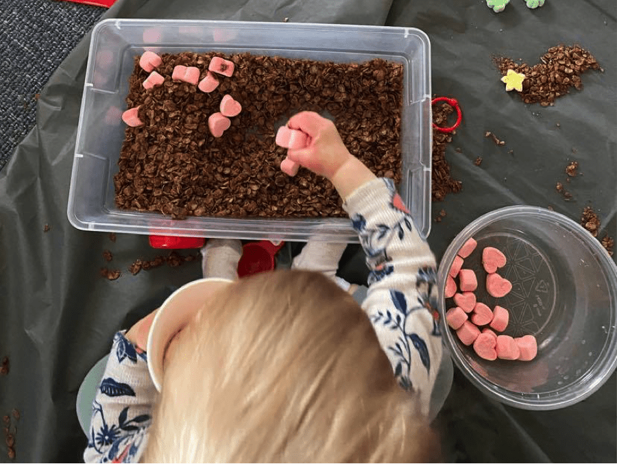 Small child putting marshmallows into Valentine's Day Sensory bin
