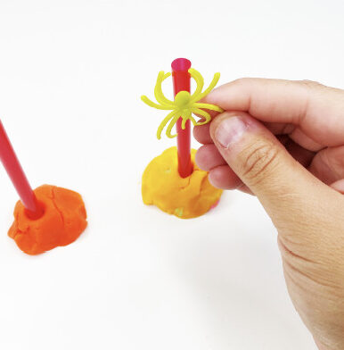 student using the stack it fall fine motor center and putting a spider wring on a straw that is in a ball of play dough