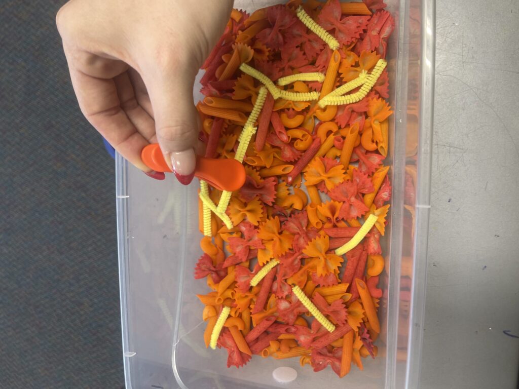 Sunny themed weather sensory bin using red and orange noodle, yellow pipe cleaners, and a pincher grasp tool.