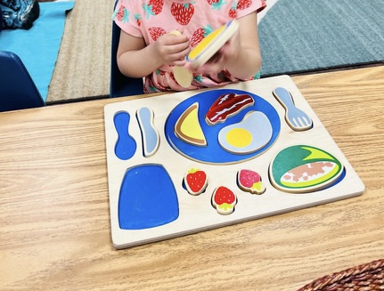 A student playing with a table setting puzzle. Puzzle help with fine motor skills and Language