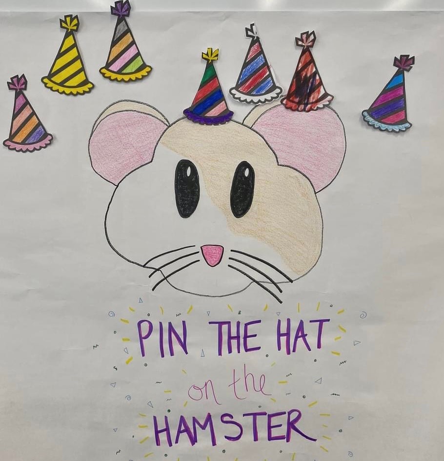 A white poster with a drawing of a tan and white hamster face. There are colorful paper party hats above the hamster's head.