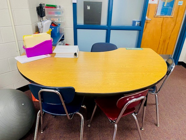 A brown wooden kidney table is shown next to a door in a classroom.
