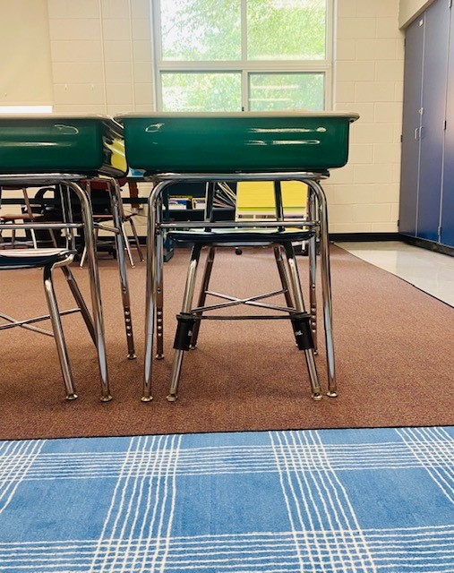 A student desk in a classroom, with a black bouncy band on the chair.