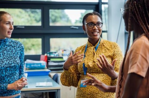 Three adult women standing in a classroom, talking.