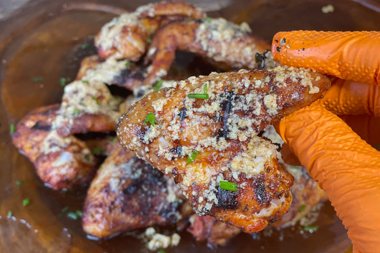 a cooked wing with sauce being held above a plate of wings