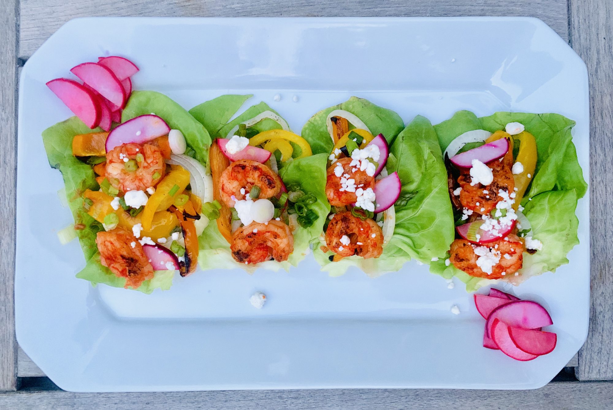 Picture of a white platter full of color brimming from the buffalo shrimp lettuce wraps topped with crumbled goat cheese. For more recipes and travel blogs check out www.sprouting-vitality.com #kenzinthekitch #sproutingvitality #mckenzieonthemove
