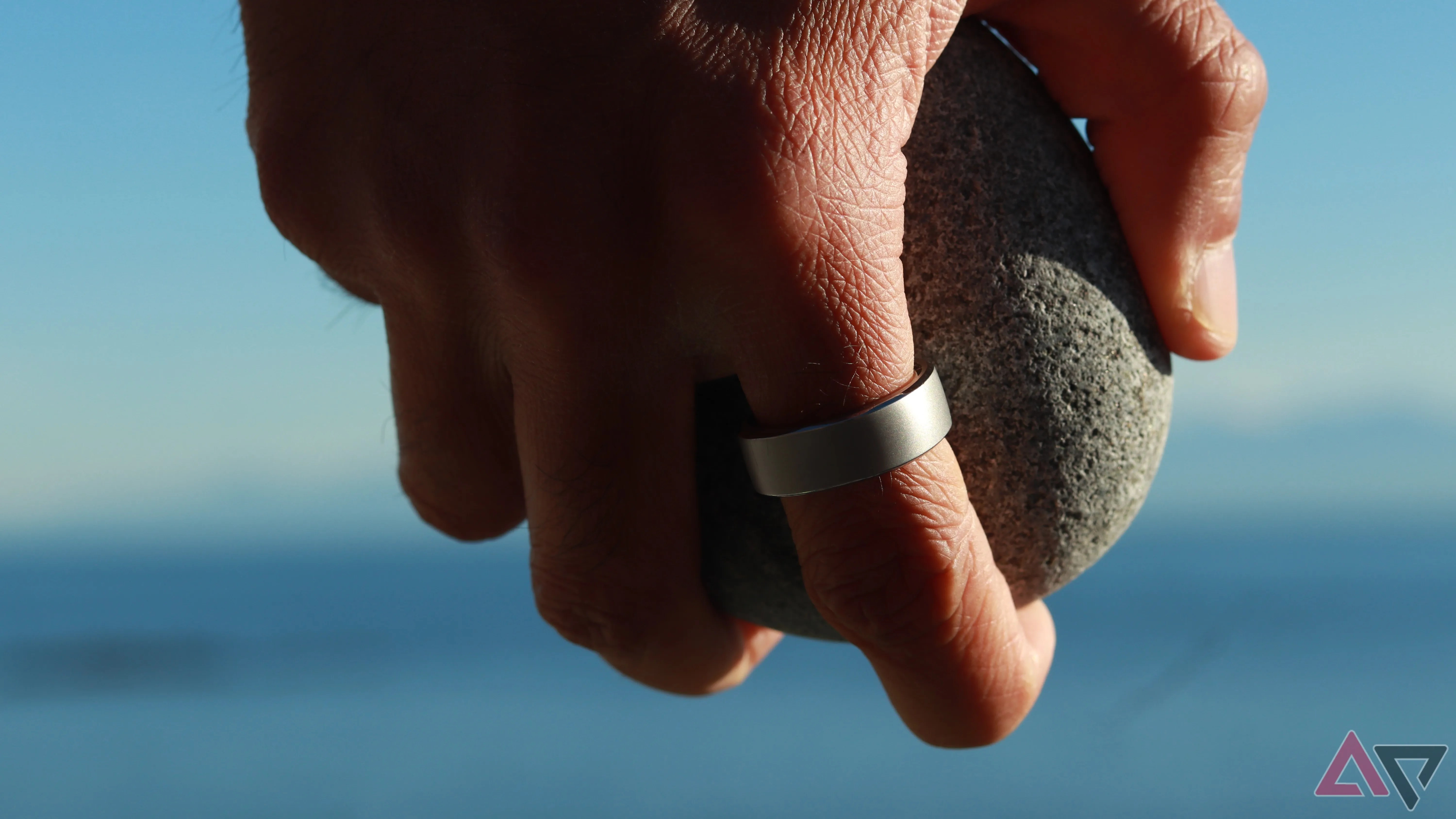 A hand wearing a smart ring holding a rock
