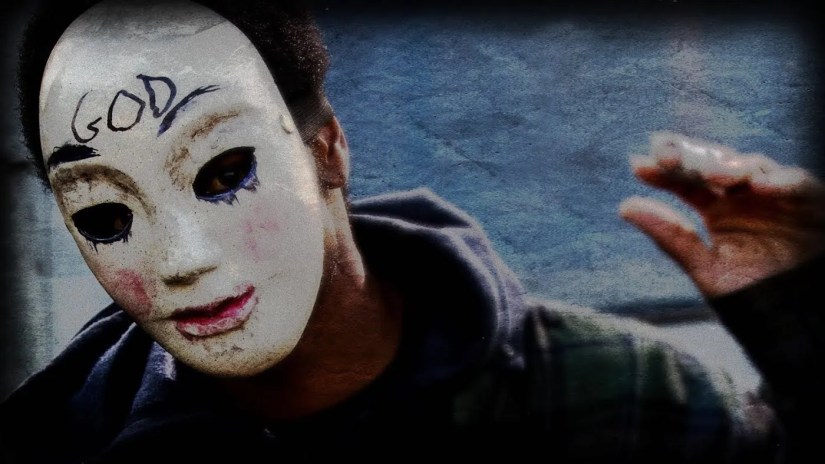 Still from &lsquo;&lsquo;The Purge: Anarchy&rsquo;: a man wearing a mask with &lsquo;God&rsquo; written on it waves sinisterly.