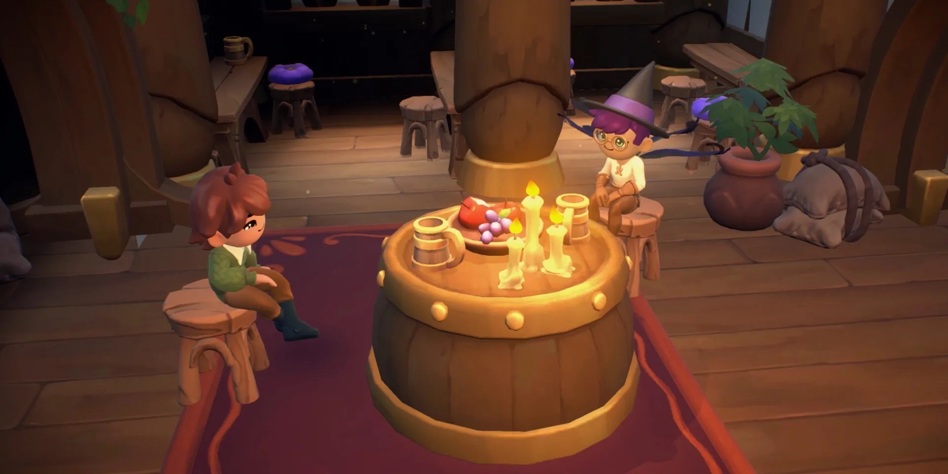 Two individuals, one of which is in a witch&rsquo;s hat, sitting on stools on either side of a barrel table with candles, mugs, and a fruit platter on it in Fae Farm