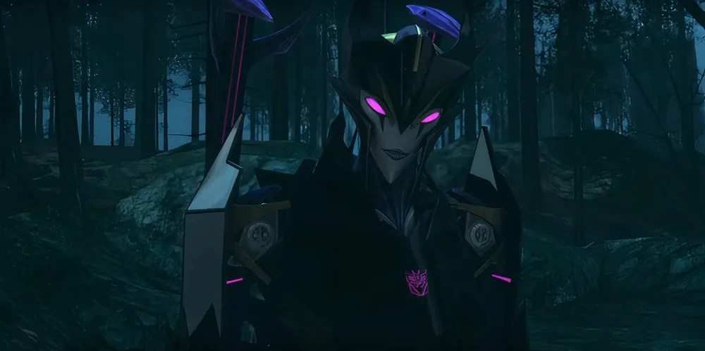 Airachnid in a forest. Her eyes glow purple, and she is smirking. Image source: Transformers Official YouTube