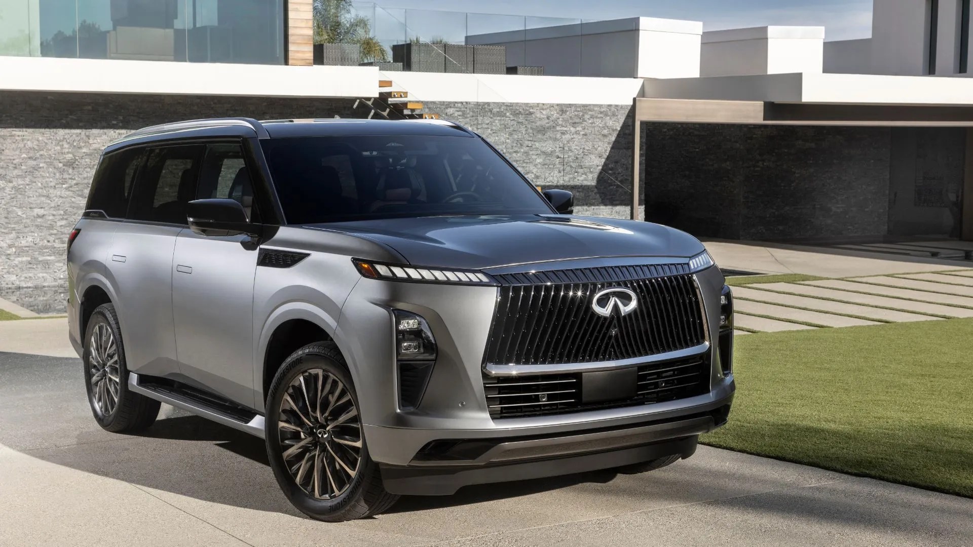 Static front 3/4 shot of a gray 2025 Infiniti QX80 parked outside of a house.