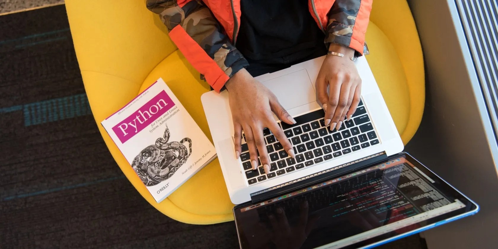 Hand typing on PC with Python coding book on the side