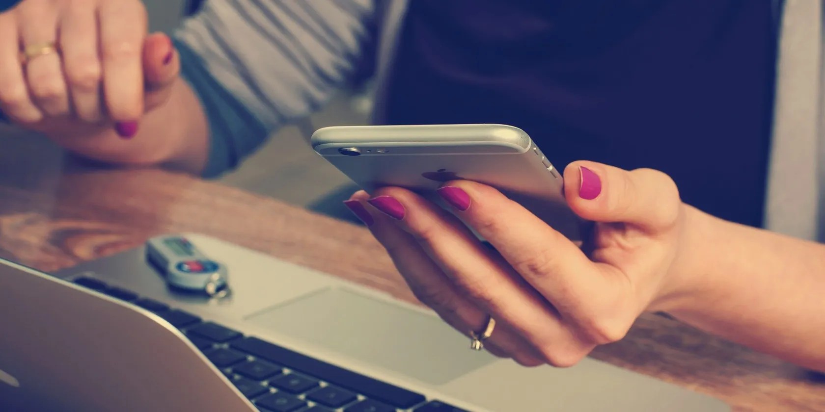 Person Holding Smartphone with wooden desk and silver laptop