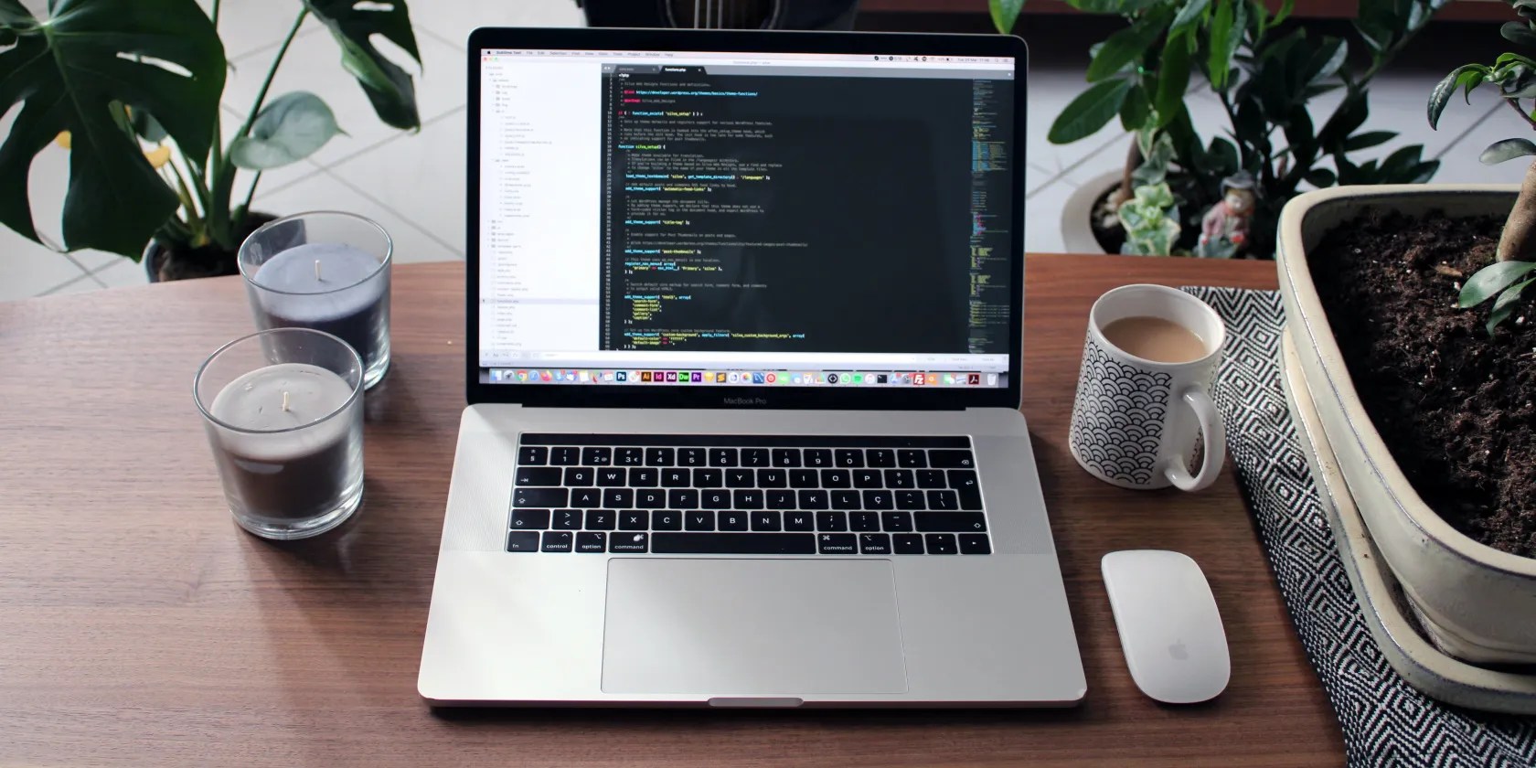 A laptop computer on a coffee table with near a coffee cup, candles, and plants