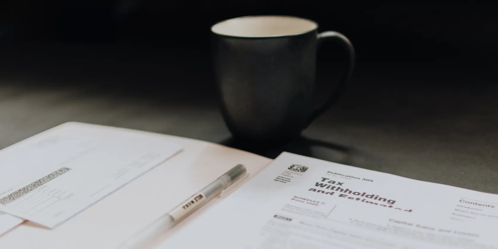 A coffee cup sits behind some tax forms on a table