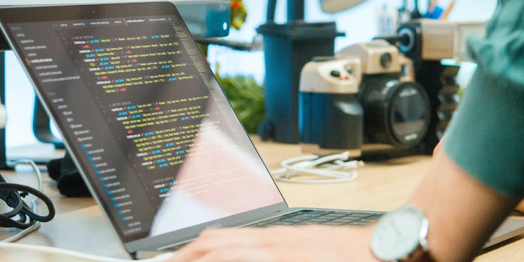 An open laptop showing colored code on a dark screen with the user’s arm visible in the foreground.