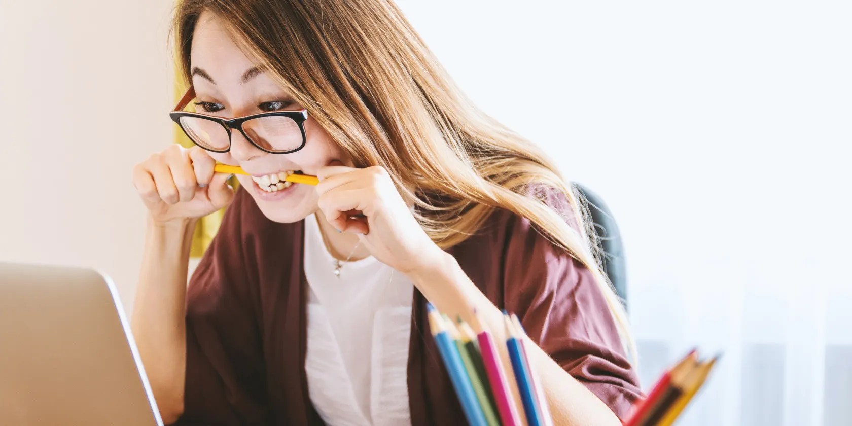 Woman biting pencil while doing work on her computer.