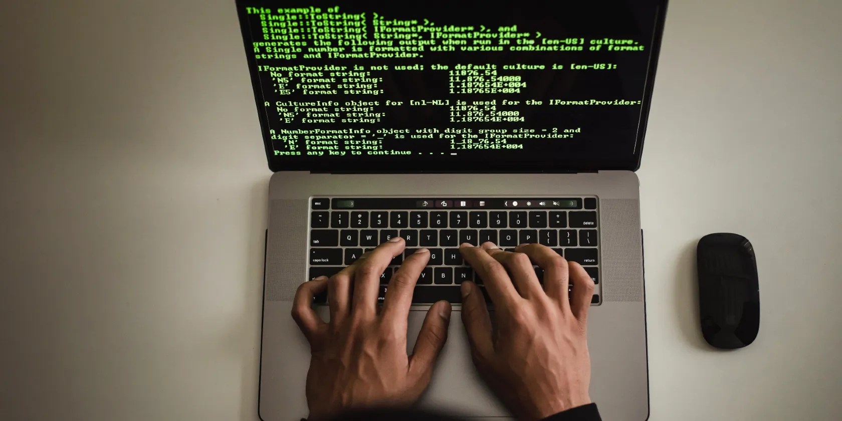 A view from above of hands typing on a laptop with green programming code shown on-screen