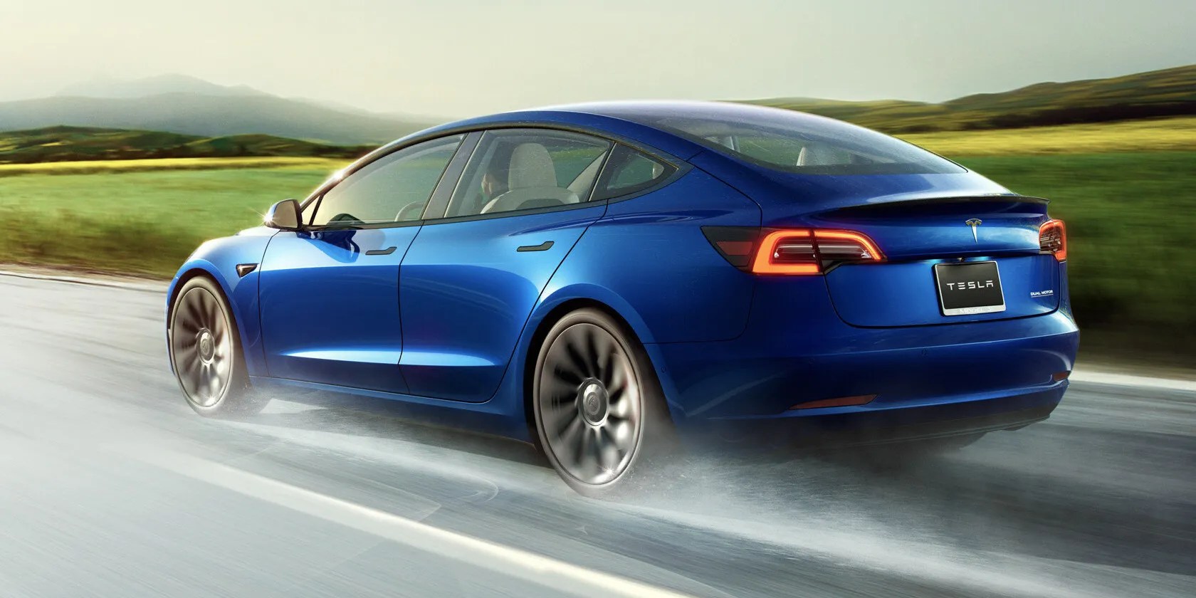 A blue Tesla Model 3 braking on a wet roadway