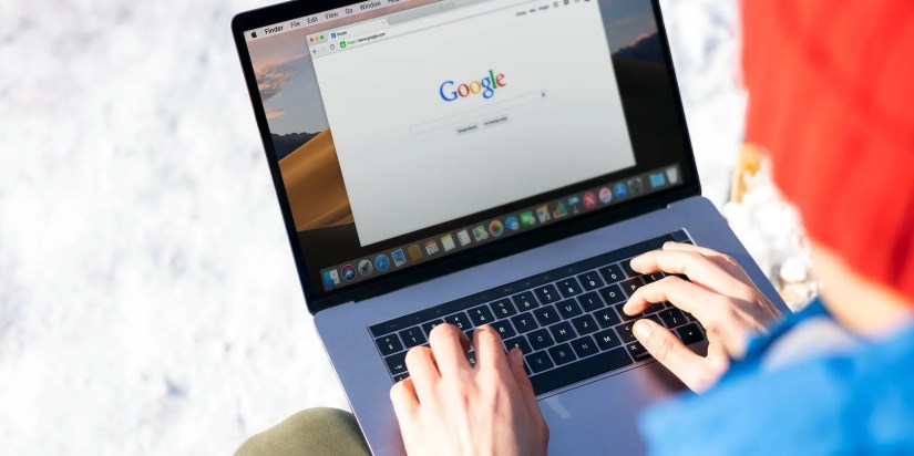 A person using a MacBook Pro with Google website on screen.