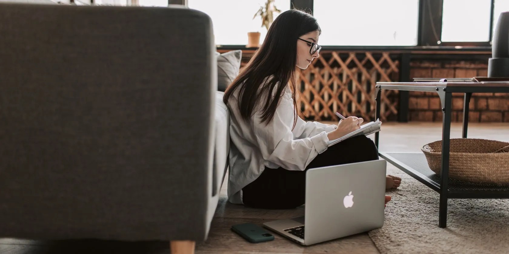 A woman writing in a notebook next to a MacBook
