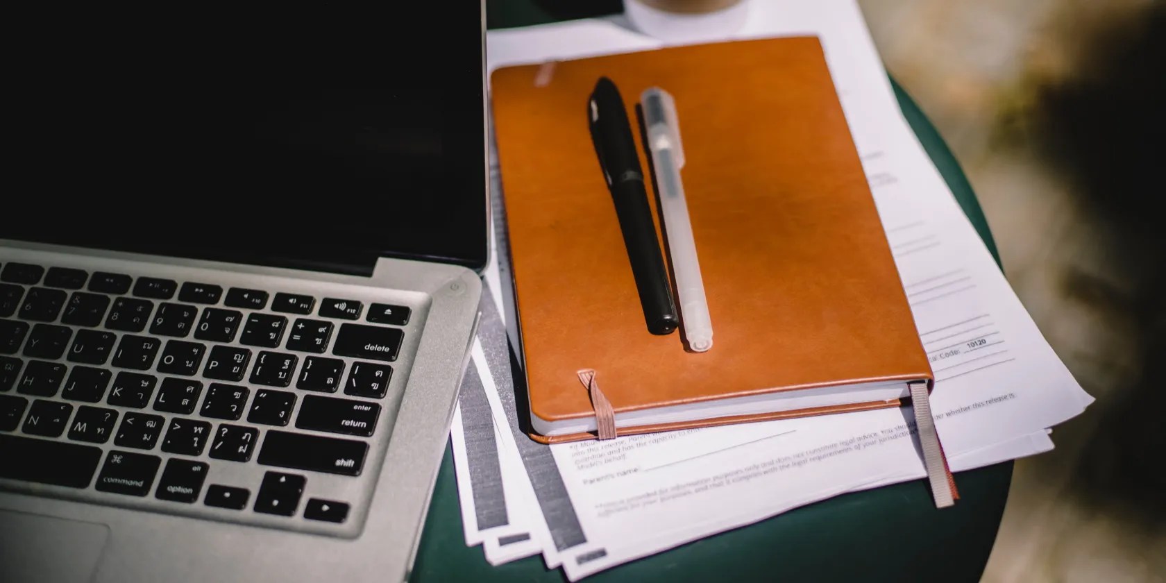A MacBook, notebook, few pieces of paper, and two pens.