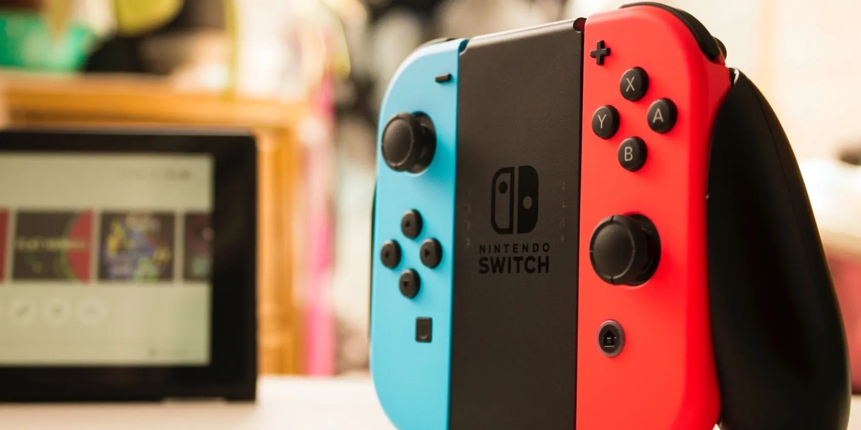 A photograph of Nintendo Switch Joy Cons attached to their cotroller adapter and set up in front of the Switch Display